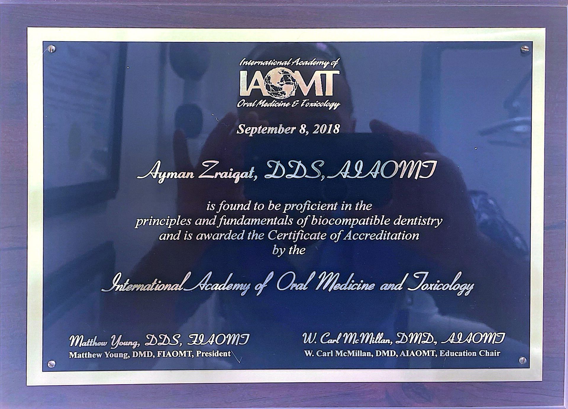 A plaque certifying Ayman Zraigat for proficiency in biocompatible dentistry, awarded by the International Academy of Oral Medicine and Toxicology.